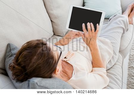 Woman using digital tablet while resting on sofa at home