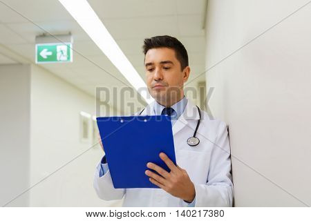 medicine, healthcare and people concept - doctor writing to clipboard at hospital