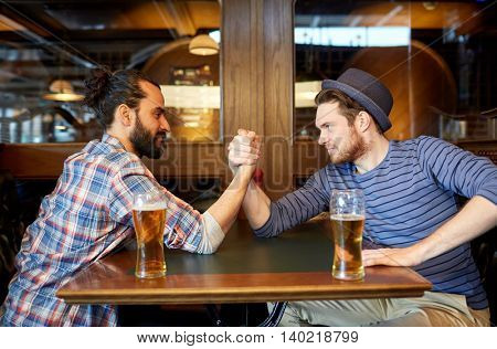 people, leisure, friendship and party concept - happy male friends drinking draft beer and arm wrestling at bar or pub and