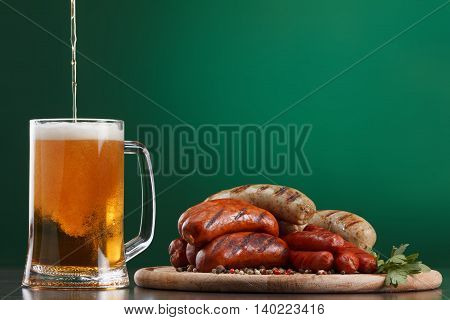 Traditional Oktoberfest menu. Beer being poured into a glass with foam traditional snacks sausages grilled. Copyspace with green background
