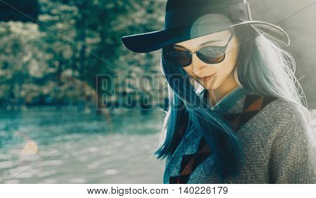 Beautiful young woman in hat and glasses resting on lake in summer outdoor. Toned image