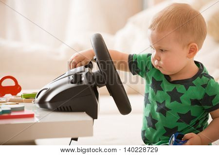 Cute little toddler boy playing with Computer steering wheel. Future driver. Getting ready for professional driving. Child driving a car. Funny toddler boy indoors. Boy and a car.