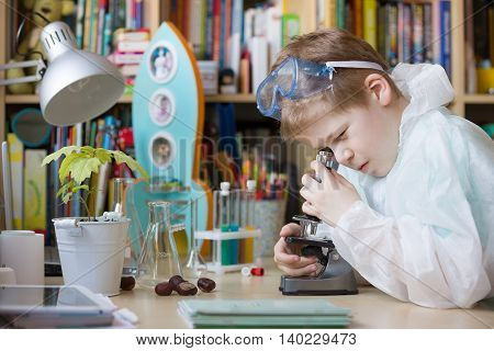 Cute elementary school boy looking into microscope at his desk at home. Young scientist making experiments in his home laboratory. Indoors. Child and science.