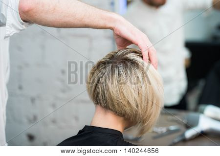 Closeup portrait teen young girl woman sitting in chair in hair salon looking in mirror while hairdresser checking her new haircut.