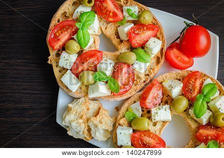 Italian starter friselle. Classical frisella tomato cheese mozzarella olives and basil with oregano and olive oil. Dried bread called freselle on white plate. Italian food. Healthy vegetarian food.