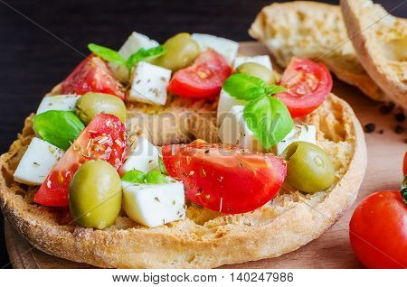 Italian appetizer Friselle. Italian dried bread Friselle on wooden board with tomatoes cherry basil and olives. Italian food. Healthy vegetarian food. Selective focus.
