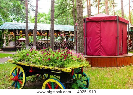 The cart with flowers. Scarlet red geranium flowerbed in retro styled old wooden wagon with birch firewood. Cranesbill in park landscape design, modern landscaping