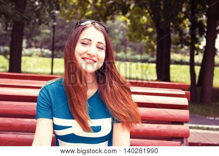 Beautiful model sits on a bench in the Park. Summer