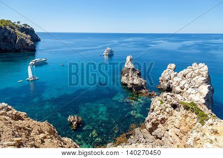 Azure bay with crystal clear water which offers incredible views of the vast expanses. Lonely sailer rock on the waves and go into the distance cruise liners. Mallorca. Spain