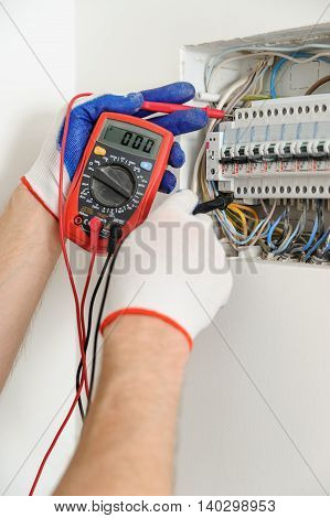 Electrician check voltage in electrical fuse box with a multimeter.