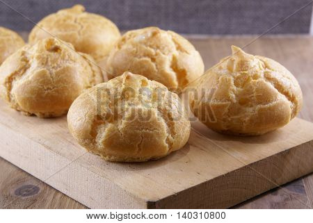Cakes profiteroles lie on a chopping board, which lies on a rustic wooden table