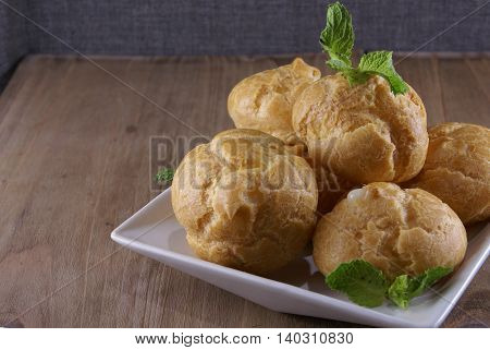 Cakes profiteroles decorated with mint leaves lying on a rustic wooden table