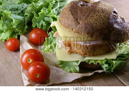 Picnic, sandwich with meat, cheese and fresh vegetables is lying on a rustic wooden table.