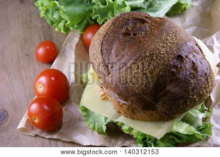 Picnic, sandwich with meat, cheese and fresh vegetables is lying on a rustic wooden table.