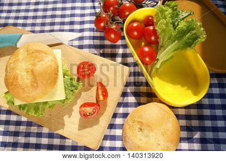 Cooking lunchbox. Homemade cheeseburger, sliced tomato on the board, knife on the board; vegetables lie in a box for lunch.