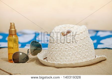 Summer vacations concept. Beach accessories. Straw hat sunglasses sun oil and blanket on sand.