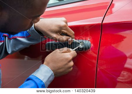 Young Male Mechanic Holding Lockpicker To Open Red Car Door