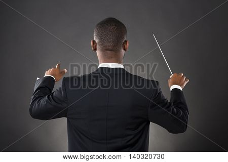 Young African Conductor Directing With His Baton Against Black Background