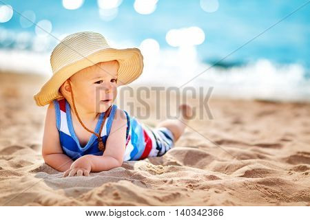 one year old boy lying the beach in straw hat. Child resting at the sea