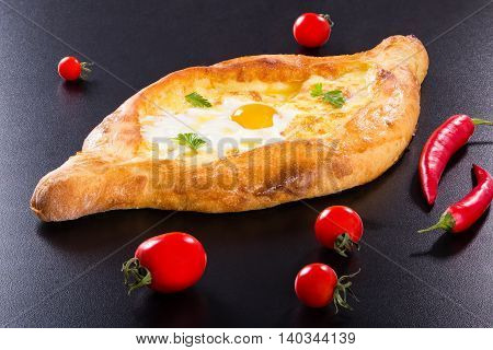 Ajarian khachapuri with egg on black background with cherry tomatoes and red chili pepper authentic recipe view from above close-up