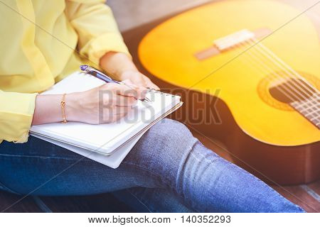 Closeup Songwriter Writing On Note Paper With Acoustic Guitar Near By.