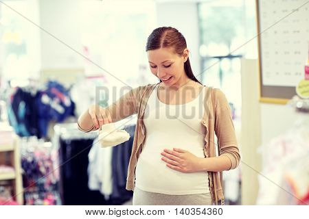 pregnancy, people, sale and expectation concept - happy pregnant woman shopping and buying baby baby bootees at children clothing store