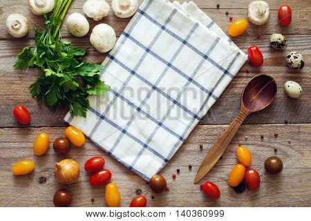 Raw cooking ingrediets (cherry tomatoes, pepper, onion, parsley, mushrooms, quail eggs) and kitchen cloth on rustic wooden table. Top view with copy space for text