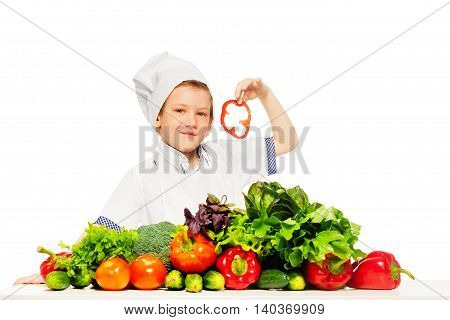 Kid boy playing chef cook preparing fresh salad holding slices of red pepper, isolated on white