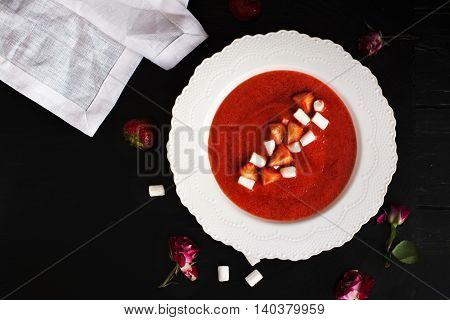 Delicious strawberry soup with marshmallows and berries over black wooden background