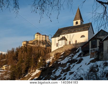 Small rural church and castle on the background in Tarasp village, Graubunden, Switzerland