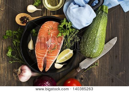 Raw salmon steak in an iron skillet with ingredients for healthy dinner. Top view
