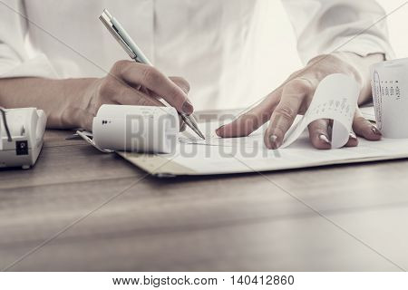 Businesswoman or accountant working at her desk correlating and checking figures on an adding machine retro effect faded look.
