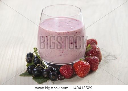 Smoothies of black currant and strawberries with yogurt on a wooden table.