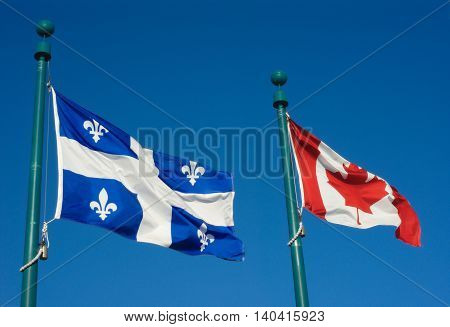 Quebec and Canada flags fluttering in the wind together on blue sky