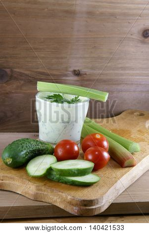 Useful summer snack: vegetables and yogurt sauce with herbs. Against the background of a rustic wooden table