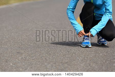 young woman runner tying shoelace on road