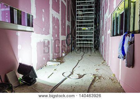 Searchlight is sheds light on mobile scaffold placed in long corridor made of plasterboard.