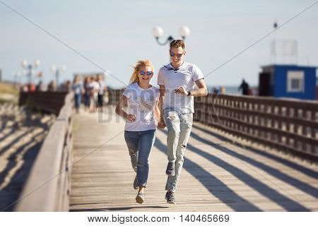 Cheerful couple are running along the boardwalk at summer time