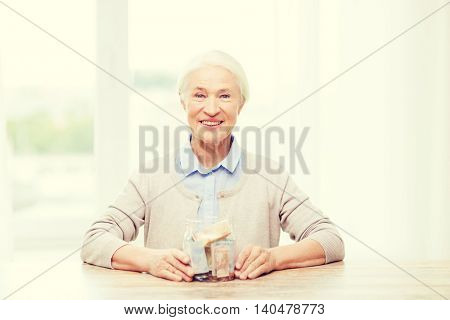 savings, money, annuity insurance, retirement and people concept - smiling senior woman with money in glass jar at home