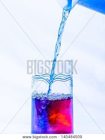 Water glass with red dye being filled with from a pitcher with blue dye.