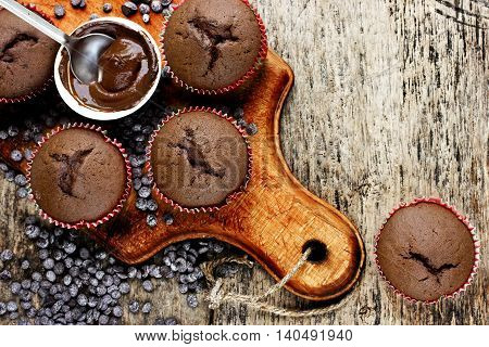 Chocolate muffins and melted chocolate on wooden table with chocolate chips top view blank space for text