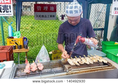TOKYO JAPAN - 18 JULY 2016 - Street vendor man cooks fish on sticks at Tsukiji Fish Market in Tokyo Japan on July 18 2016