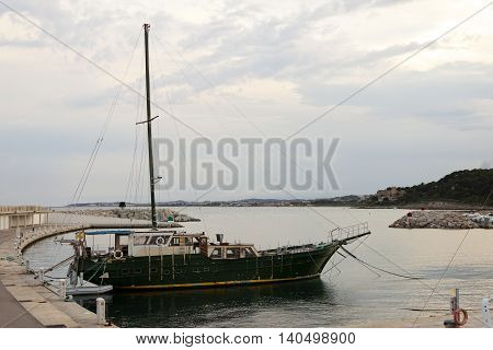 Green wooden vintage vessel moored in the pier in Roc de Sant Gaieta Tarragona Spain. The yacht is old and rusty with peeling paint.