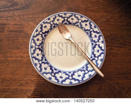 Blue flower clay plate and steel fork on wooden floor.