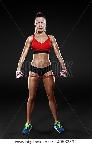 Shot of young female exercises with a jump rope looking at the camera. Muscular woman with skipping ropes against black background, with clipping pach, isolated.
