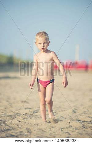Baby boy walking on the sandy beach near the sea. Cute little kid at sand tropical beach. Ocean coast.