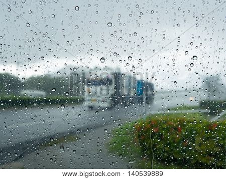 Rain water drop on mirror wall after rainy with blur truck driving on road and fresh green plant on wayside in background. Safety driving on road in rainy concept.