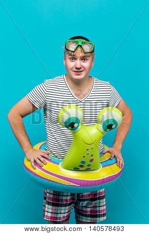 Man with an underwater mask, striped shirt, swimming laps in the form of a snail looking into the camera, blue background. Vacation concept