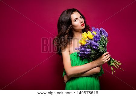 Long-haired seductive brunette with bouquet of flowers. Vinous background. Isolated