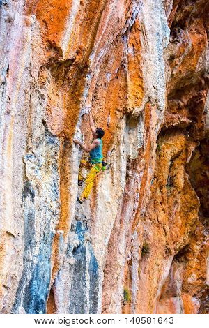 Mature male Climber makes difficult Move leading multi pitch route on colorful orange and blue rocky Wall